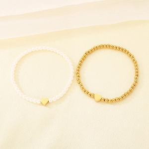 Detail of French retro pearl and gold bead bracelets with heart charms on cream fabric.