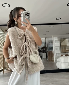 Detail view of beige plush vest featuring three large decorative bows and lace-up front styling