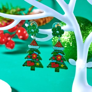 Detail of glitter Christmas tree acrylic earrings hanging on a white antler jewelry stand