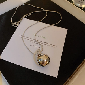 Detailed view of silver water drop pendant on a sleek snake chain against a white card