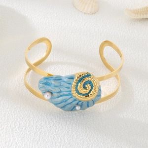 Detailed close-up of a gold pearl shell bangle featuring ocean-themed blue enamel accents