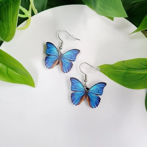 Detailed close-up of blue butterfly wing bridal earrings on a white circular plate