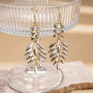 Detailed view of gold leaf-shaped earrings with sparkling crystals on textured glass