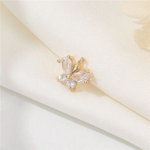 Detailed macro view of 14k gold plated butterfly charm with cubic zirconia inlay on white fabric
