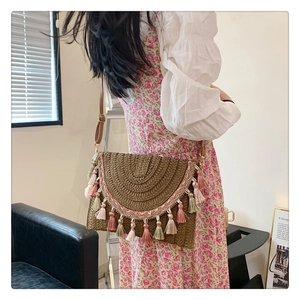 Detail of woven straw crossbody bag featuring colorful tassels and brown leather strap