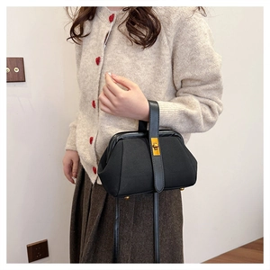 Retro black shell-shaped handbag with golden buckle worn on a beige cardigan