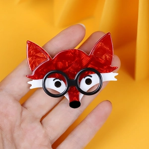 Handcrafted red and white acrylic fox brooch with black glasses on a fabric background