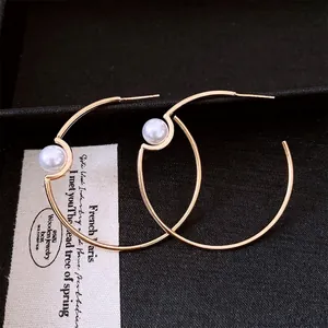 Minimalist gold-plated hoop earrings with white pearl detail on black leather background