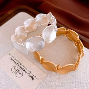 Detail of wave-shaped matte gold and silver alloy bracelets on a beige fabric surface