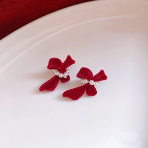 Detail of red flocked bow earrings with a central pearl on a white background