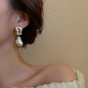 Macro detail of retro rose earrings with baroque pearl drop worn by a model