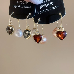 Détail de boucles d'oreilles cœur et perle en argent 925 avec chaîne dorée et gemmes