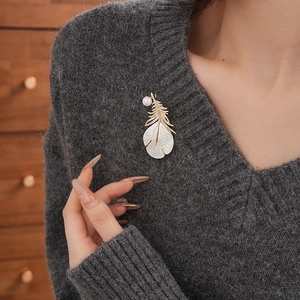 Detail of gold羽毛brooch with zircons and mother of pearl on dark sweater