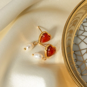 Detail of heart-shaped earrings with red agate and pearls on a silk background