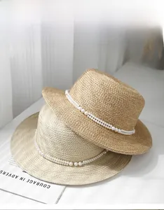 Top view of flat-top straw boater hats with elegant pearl strap detail in a sunlit setting