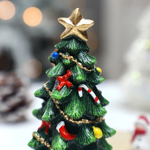 Miniature green resin Christmas tree with gold star and red bows on a bokeh background