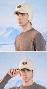 Detail of winter knit earflap cap with leather logo patch against a snowy mountain backdrop
