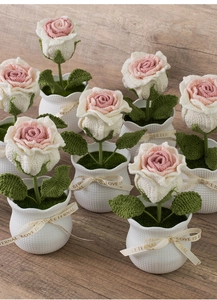Close-up of handmade crochet rose plant with pink petals and green moss in a textured pot