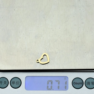 Detailed view of a small golden hollow heart pendant on a scale weighing 0.71 grams