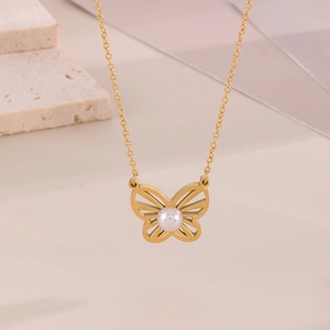 Close-up of golden butterfly pendant necklace with pearl inlay on minimalist stone props