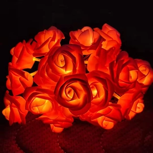 Close-up of red rose LED string lights glowing with warm orange light in the dark