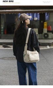 Detailed side view of a large cream-colored nylon messenger bag worn by a model
