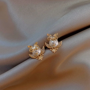 Macro detail of owl stud earring in gold metal with white pearl and sparkling crystals