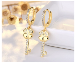 Detail of gold clover key earring with white cubic zirconia on a white plate