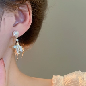 Détail de boucle d'oreille perle avec pétales en émail blanc et accents dorés sur modèle