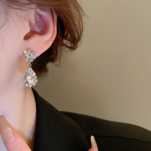 Close-up of silver drop earrings with sparkling crystals worn by a model in soft lighting