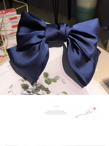 Detailed view of large dark blue satin bow hair clip on a stylish decorative shelf