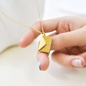 Close-up of a gold envelope pendant necklace with fine chain detail on model's hand