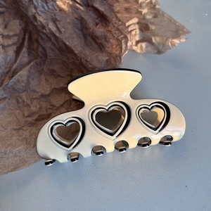 Detail of a large cream acetate hair claw with hollow heart designs and black outlines
