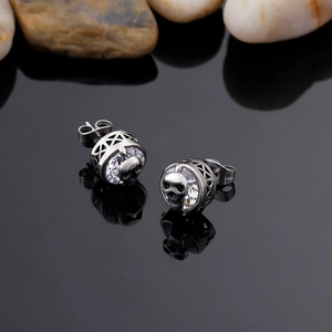 Detail of silver skull stud earring with large clear zircon and polished metal texture