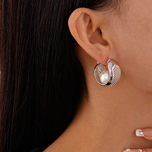 Detail of a mesh metal hoop earring with a white pearl on a model for a chic look