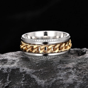 Detailed macro of silver textured ring with gold cuban chain on dark rock surface