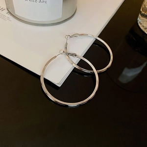 Close-up of geometric silver hoop earrings with a polished mirror finish on a minimalist desk