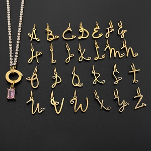 Close-up of 26 cursive gold initial charms with heart accents on a smooth black surface