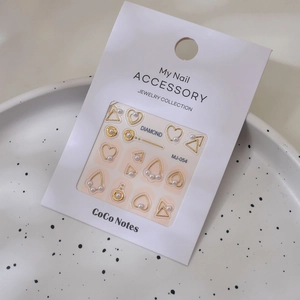 Detail shot of golden metal heart charms and pearl nail art decals on paper card