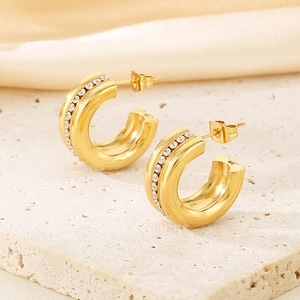 Macro shot of gold-plated C-shaped earrings with inlaid clear zircons on stone surface