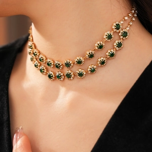 Nahaufnahme eines zweilagigen Gold-Chokers mit smaragdgrünen Edelsteinen in Blumenform