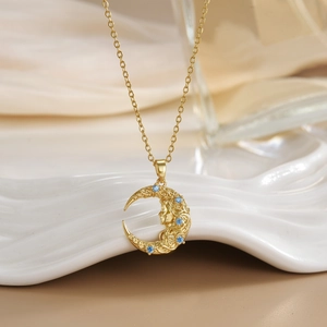 Detailed close-up of gold moon pendant with goddess face relief and blue zircon accents