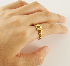 Detailed view of a gold-plated twisted croissant dome ring on a finger with a metallic texture