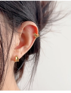Macro shot of minimalist gold ear cuff and huggie hoop earring worn on the earlobe