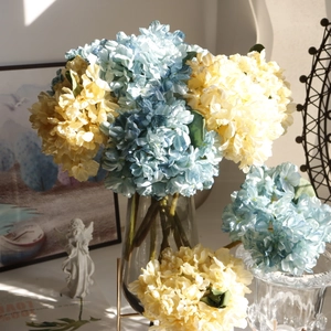 Close-up of vintage hydrangea artificial flowers in blue and yellow hues in a glass vase