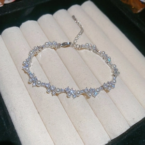 Macro shot of silver pearl bracelet with zircon clusters on beige fabric tray