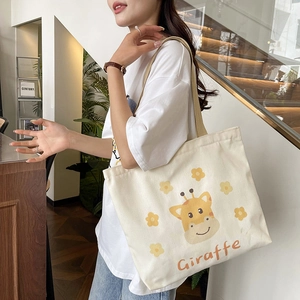 Large canvas shoulder bag with cartoon giraffe print worn by a model in a modern setting
