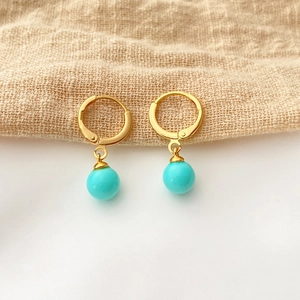 Close-up of gold-plated hoop earrings with turquoise round shell pearl pendants