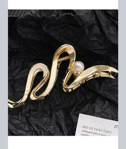 Detailed view of large gold wave-textured hair claw clip with faux pearl accent