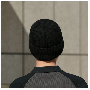 Detailed texture of black ribbed knit beanie shown on model against a gray wall